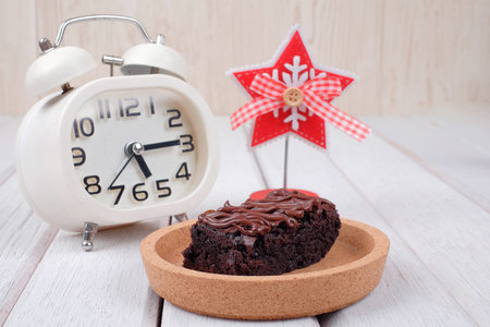 Alarm clock, note clipper and  chocolate brownie with melted chocolate on a wooden plate