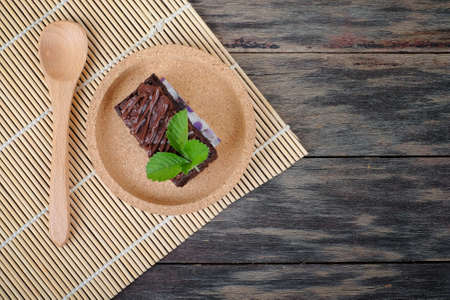 Wooden spoon and chocolate brownie with melted chocolate on a wooden plateの写真素材