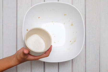 Pouring sugar into mixing bowl with ingredients for making cookiesの写真素材