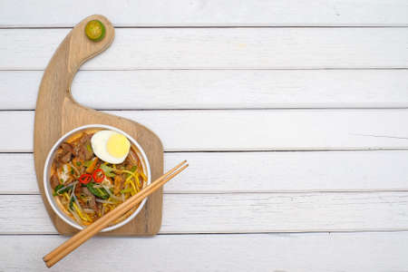 Mee Rebus in the bowl  with chopsticks on white table This dish is made of noodles ,vegetable,egg with a spicy .の写真素材
