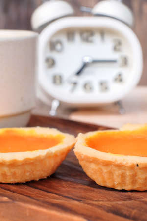 Egg tart, alarm clock  and a cup of coffee on wooden backgroundの写真素材
