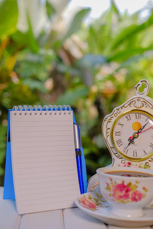 Cup of coffee, open notebook with blank pages, vintage clock, pen,  on green background  Still life,...