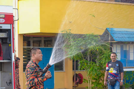 Muadzam Shah, Malaysia -  November 24th  , 2018 : Fireman flushes water towards Muadzam Shah's children at a mass circumcision ceremony in the yard of  school during long break of school holiday.のeditorial素材