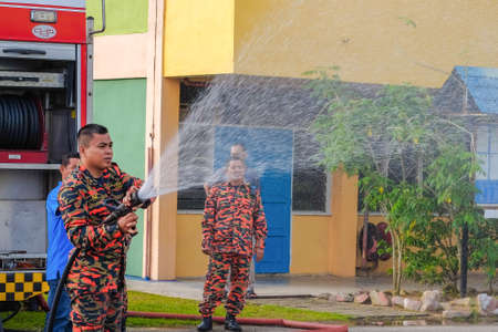 Muadzam Shah, Malaysia -  November 24th  , 2018 : Fireman flushes water towards Muadzam Shah's children at a mass circumcision ceremony in the yard of  school during long break of school holiday.のeditorial素材