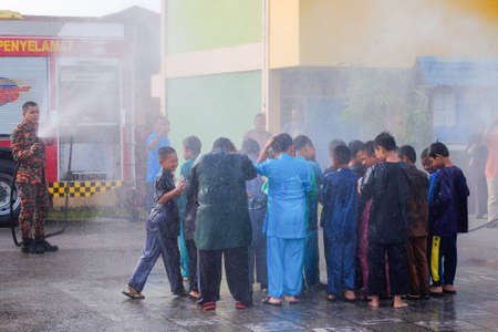 Muadzam Shah, Malaysia -  November 24th  , 2018 : Fireman flushes water towards Muadzam Shah's children at a mass circumcision ceremony in the yard of  school during long break of school holiday.のeditorial素材