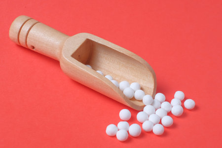 White pills and wooden scoop on red background
