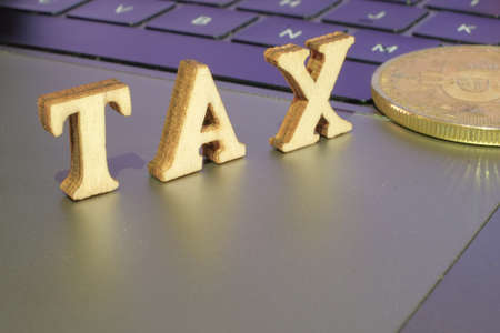 Bitcoin  and next to wooden with TAX letters. Bitcoin taxation conceptの写真素材