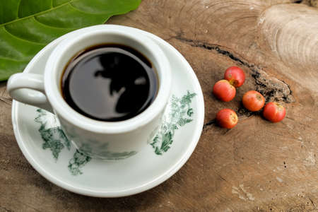 Hot coffee cup with fresh organic red coffee beans and the coffee leaf on the wooden table .の写真素材