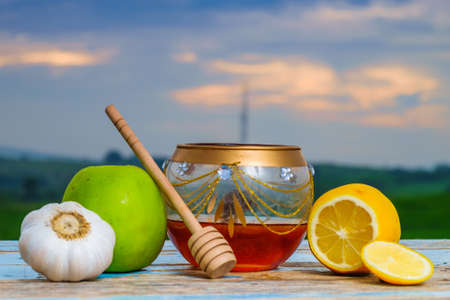 Fresh honey in glass jar, honey dipper , green apple, garlic and lemon on old wooden with blurred background , healthy nutrition and strengthening immunity .の写真素材