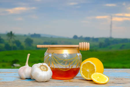 Fresh honey in glass jar , garlic and lemon on old wooden with blurred background , healthy nutrition, strengthening immunity and treatment of fluの写真素材