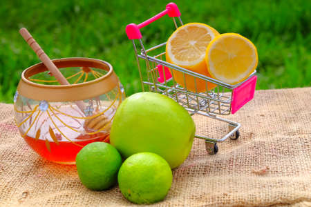 Sweet honey in the jar, shopping cart, lime  and green apple with blurred background. Conceptual image of buying vegetables and healthy eating.の写真素材