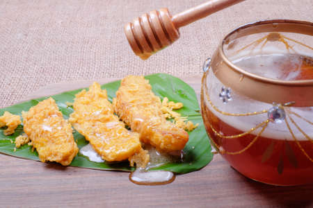 Honey dripping from wooden honey dipper and fried slices of the ripe BANANA also called Pisang Goreng, which are eaten as snack or used to accompany dishes in Malaysiaの写真素材