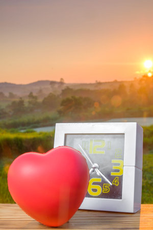 White alarm clock and red heart with nature light in the morning