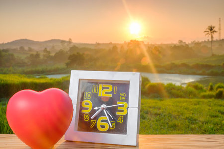 White alarm clock and red heart with nature light in the morning