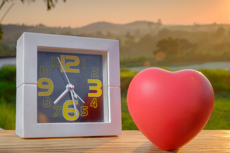 White alarm clock and red heart with nature light in the morning