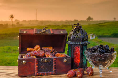Lighting Ramadan Lantern , black raisin  and  dates    on old wood with a beautiful sunrise as background. Holy month of Ramadan concept.の写真素材