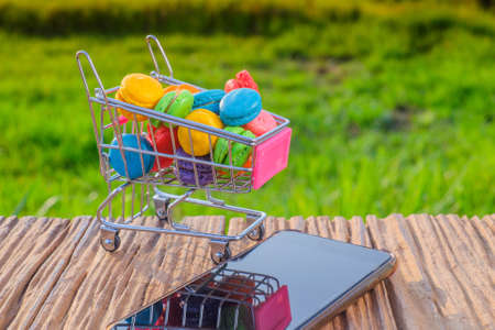 Macarons in small metal shopping cart and smartphone on green backgroundの写真素材