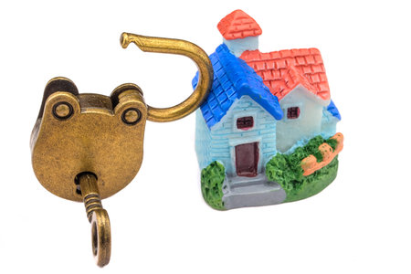 Concept of a miniature house and a golden lock with keys isolated on white background. The idea:...