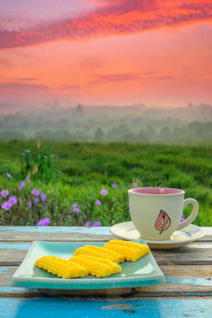 Black coffee cup and a Malay traditional cookies called Kuih Semperit  on wooden table over blurred image of beautiful scenery.の写真素材