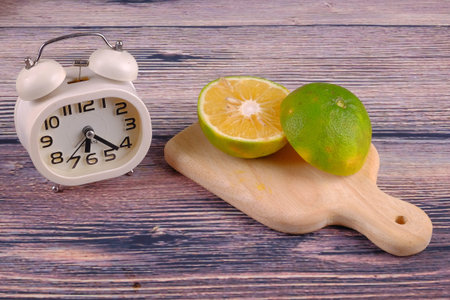 Sliced of citrus fruits and alarm clock on wood background
