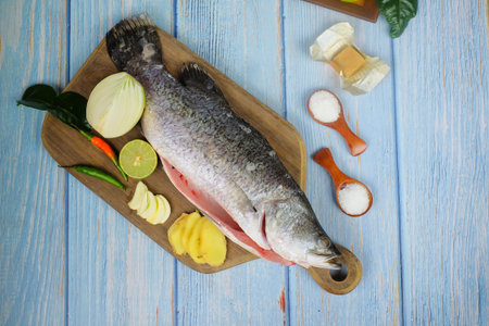 Wooden cutting board   with baramundi, salt, msg,ginger,garlic,onion,key lime, chilies,  and lemongrass over the wooden background.の写真素材