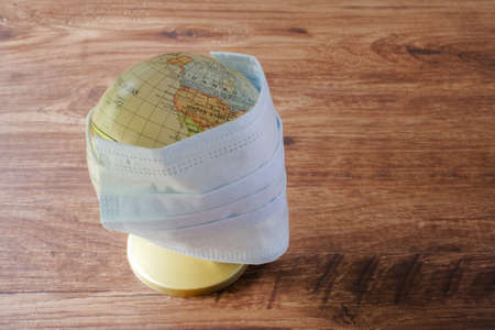 Globe  and face mask on wooden table. Covid-19 Coronavirus Outbreak conceptの写真素材
