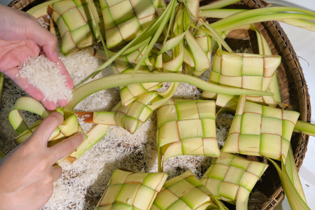 Hands filling rice into Ketupat casing. Ketupat is a local delicacy during the festive season in...