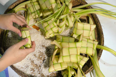 Hands filling rice into Ketupat casing. Ketupat is a local delicacy during the festive season in South East Asia. Selective focus.の写真素材