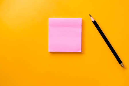 Black  pencil and pink note paper on yellow backgroundの写真素材