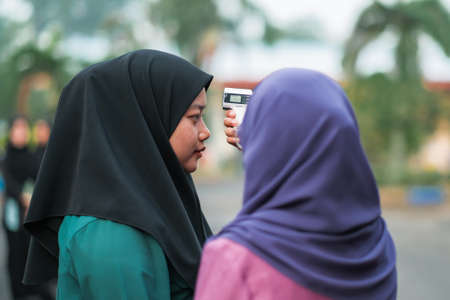 Muadzam Shah, Malaysia- July 9th, 2020:  Teacher using thermometer temperature screening student for fever against the spread of COVID-19 while student coming back to school, Education concept.のeditorial素材
