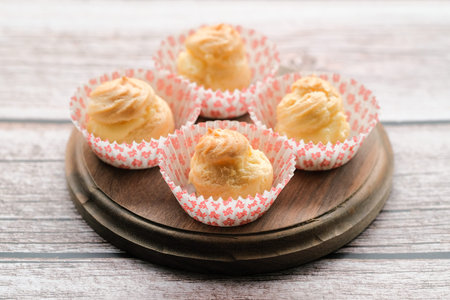 Cream puff cakes with custard on wooden background