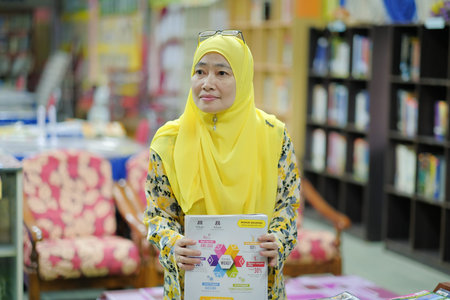 Muadzam Shah, Malaysia - August 12th, 2020 :  Cheerful mature librarian posing holding books.
