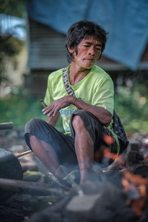 Muadzam Shah, Malaysia - August 18th, 2020 : Indigenous Malaysian aboriginal smoking a cigarette while making a knife  for hunting.のeditorial素材