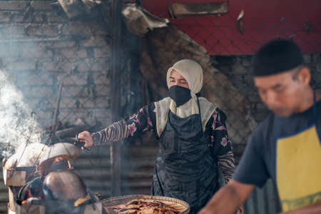 Kota Bharu, Malaysia - July 30th, 2020 : The portrait of husband and wife  making a local Malaysian desert called Akok Kedut using   coconut husks for fuel.のeditorial素材