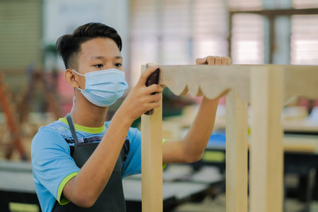 Young carpenter in work clothes and face mask  using sand paper in finishing work  for console table...