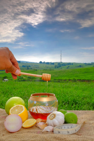 Hand with dipper picking honey from a jar of honey ,measuring tape, garlic, green apple,lime  , lime , lemon on jute with beautiful blurred background   . Healthy eatingの写真素材