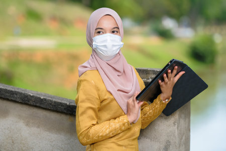 Asian muslim student woman with traditional dress wearing medical face mask at le lake.の写真素材