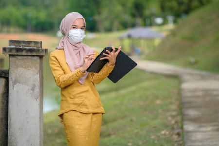 Asian muslim student woman with traditional dress wearing medical face mask at le lake.の写真素材