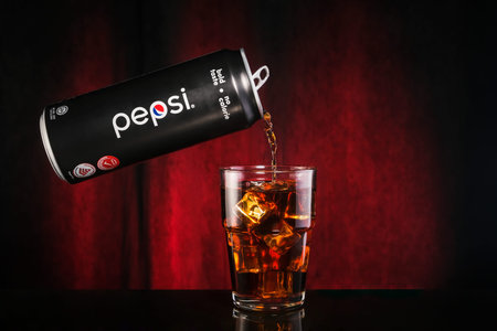 Kuala Lumpur, Malaysia - January 3rd, 2021 :  Splash pepsi into a glass on a dark red background....