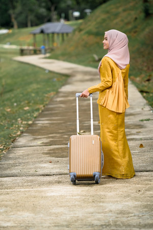Gorgeous smiling muslim woman in traditional wear holding luggage at lake garden.の写真素材