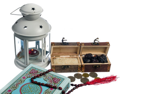 Islamic concept - The Holy Al Quran, dates , lantern, rice,coins  and prayer beads with written Arabic calligraphy meaning of Al Quran, Arabic word translation : The Holy Al Quran (holy book of Muslim), on white background.の写真素材
