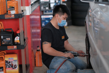 Kuala Lumpur , Malaysia - June 29th, 2020 : Car mechanic worker doing tire or wheel replacement with pneumatic wrench in garage of repair service stationのeditorial素材