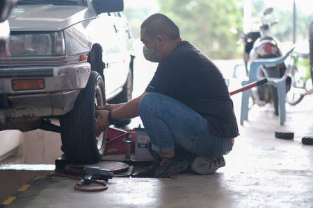 Kuala Lumpur , Malaysia - June 29th, 2020 : Car mechanic worker doing tire or wheel replacement with pneumatic wrench in garage of repair service stationのeditorial素材