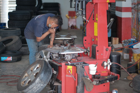 Kuala Lumpur , Malaysia - June 29th, 2020 : Tyre change on the car in a workshop by a mechanic while smoking.のeditorial素材