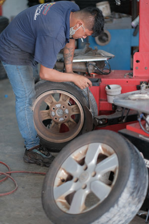 Kuala Lumpur , Malaysia - June 29th, 2020 : Tyre change on the car in a workshop by a mechanic while smoking.のeditorial素材