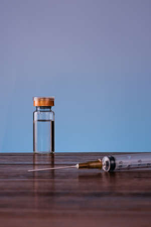 A Vaccine in vial and syringe close-up on a wooden table blue backgraund, medical concept, laboratory, subcutaneous injection vaccination, dose. Disease treatment immunization.の写真素材