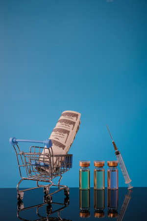 Shopping cart , syringe, money and  vaccine bottle on a blue background with place for text.の写真素材