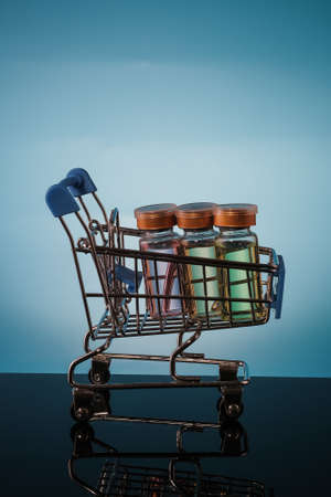 Shopping cart with vaccine bottle on a blue background with place for text.の写真素材