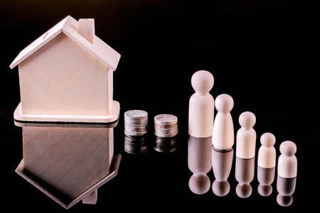 Business, Money, Finance, Home loan and management concept. Close up of wooden people figure standing on glass table with coins and mini wooden house toy on black background.の写真素材