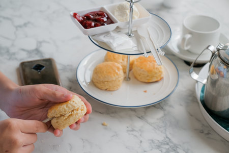 Handsome boy enjoying with scones topped with clotted cream and strawberry jam for afternoon tea ....